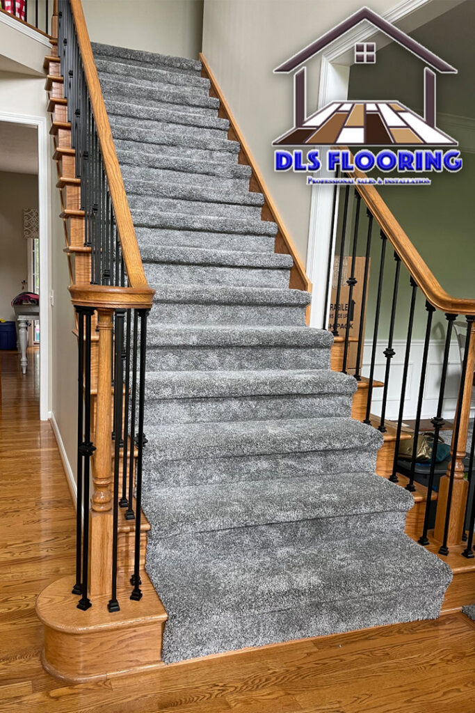 A beautifully installed grey carpet on a grand residential staircase with wooden railings by DLS Flooring in Akron, OH.
