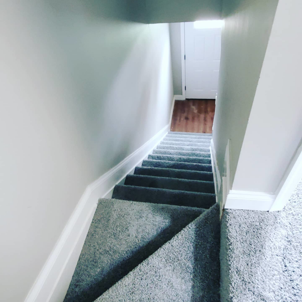 A view looking down a basement staircase with newly installed grey carpet by Yankees Carpet Inc in Baltimore, MD