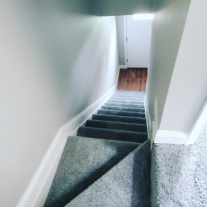 A view looking down a basement staircase with newly installed grey carpet by Yankees Carpet Inc in Baltimore, MD