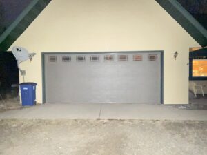 An exterior view of a grey garage door with windows on a house at night by AJK Door Services in Duluth, MN.