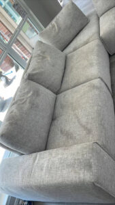 A grey sectional sofa undergoing upholstery cleaning, showing wet areas from the cleaning process by Good Guys Carpet Cleaning in Katy, TX.