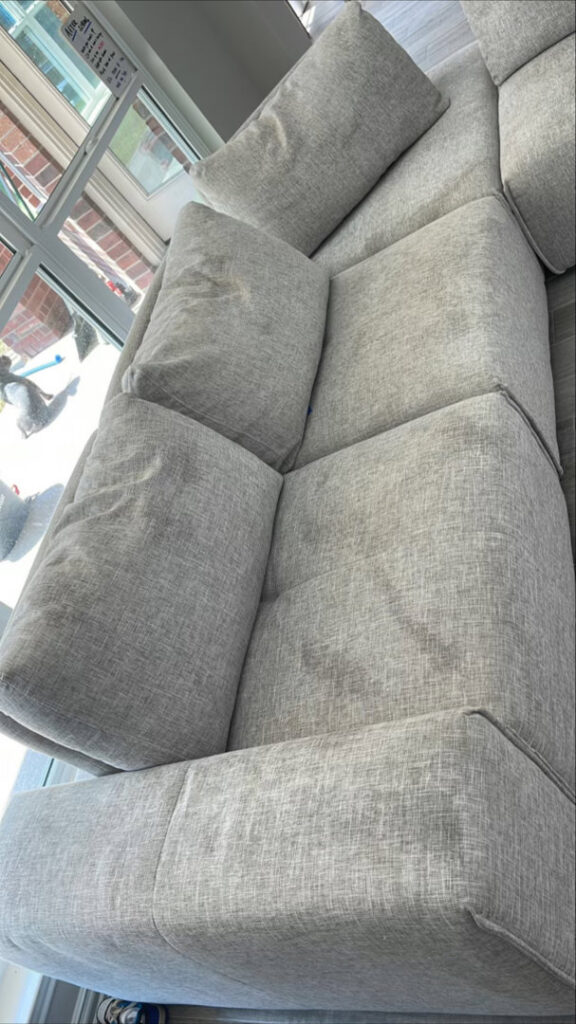 A grey sectional sofa undergoing upholstery cleaning, showing wet areas from the cleaning process by Good Guys Carpet Cleaning in Katy, TX.