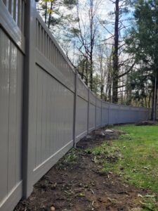 A modern grey vinyl privacy fence installed along a residential property line by Sullivan & Sons Fence LLC in Hudson, NH.