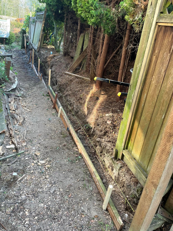Ground preparation for a new fence and retaining wall, showing a dug trench and string lines by A.T service in Kent, WA.
