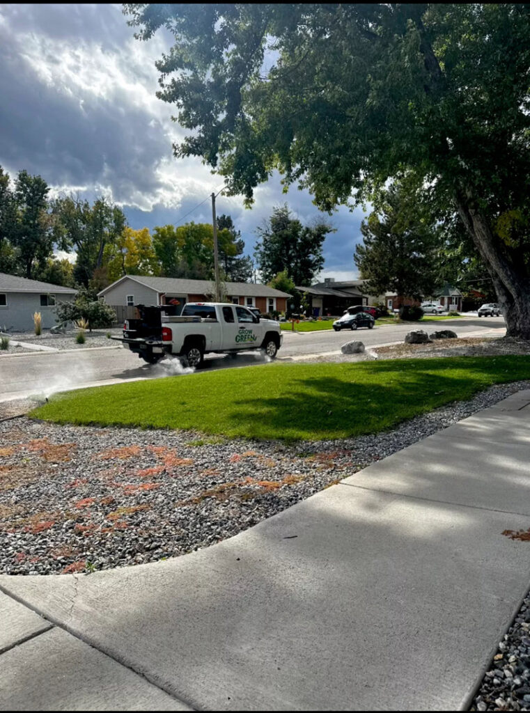 A Grow Green Irrigation Svc truck applying a lawn treatment on a residential street in Brighton, CO.