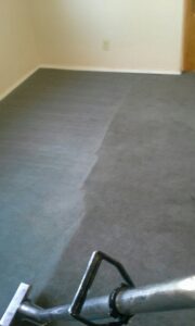 A carpeted floor showing a clear line between cleaned and uncleaned areas, with a cleaning tool, by Alex's Janitorial and Carpet Cleaning in Bakersfield, CA