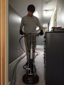A professional from Yellow Finch Carpet Cleaning LLC cleaning a light-colored carpet in a hallway with a rotary machine in Dover, NH.