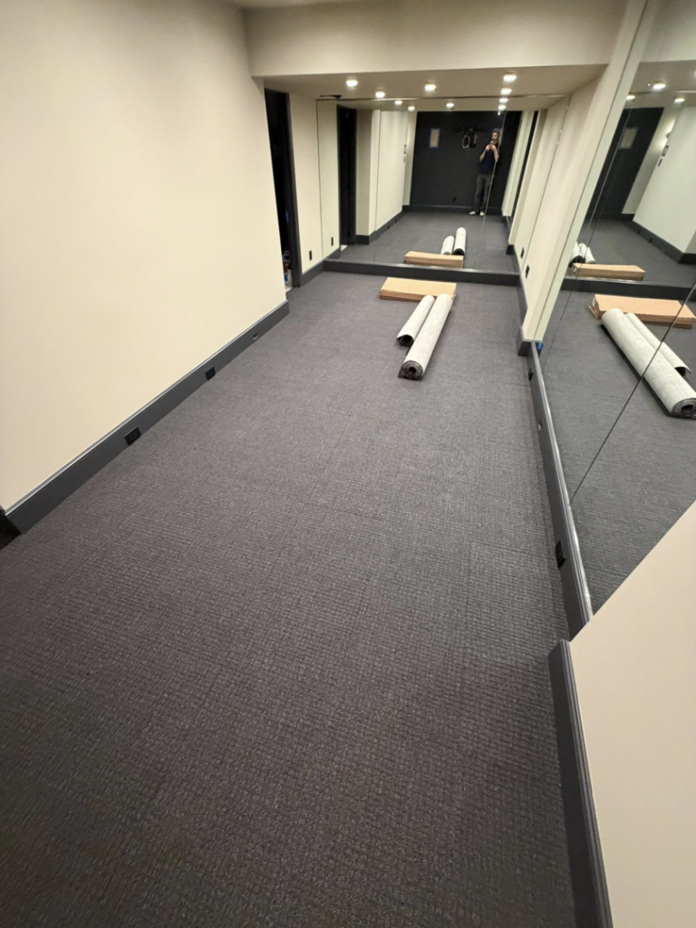 A hallway with new dark carpet installed and rolls of carpet ready for work by Good Guy Flooring in Kansas City, MO