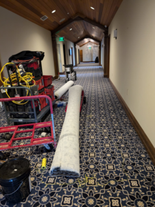 A hallway with patterned carpet being installed, showing tools and rolls by Craftmark Installations LLC in Broken Arrow, OK