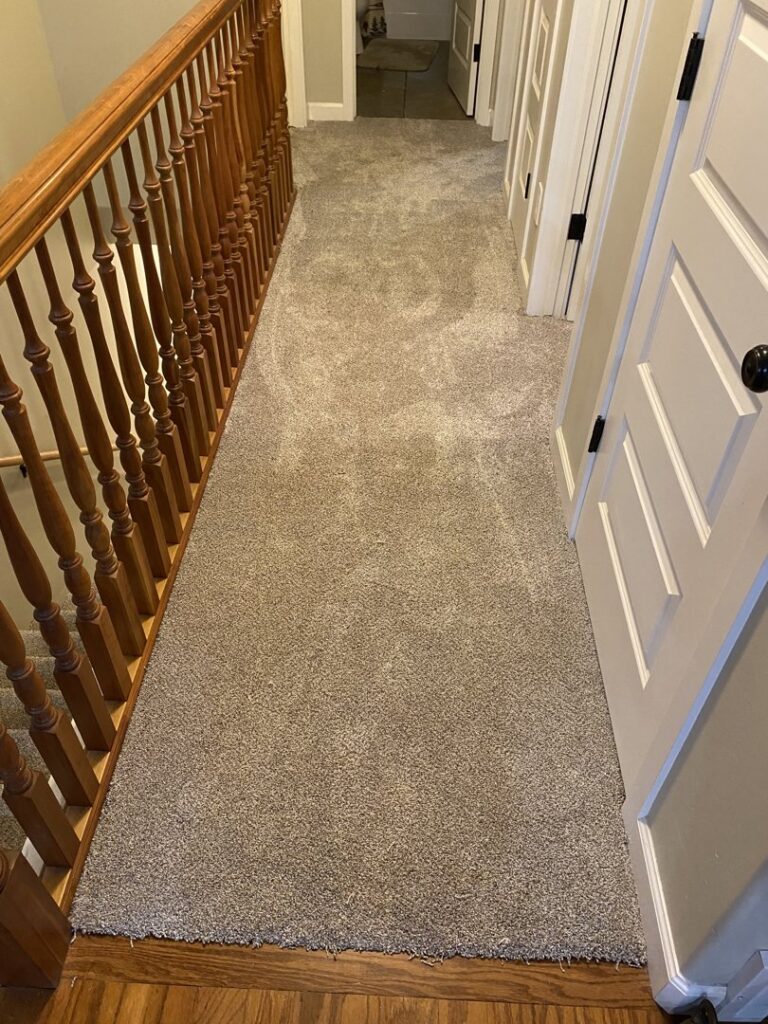 A hallway with newly installed light brown carpet and a wooden railing by IDF The Floor Store in Idaho Falls, ID.