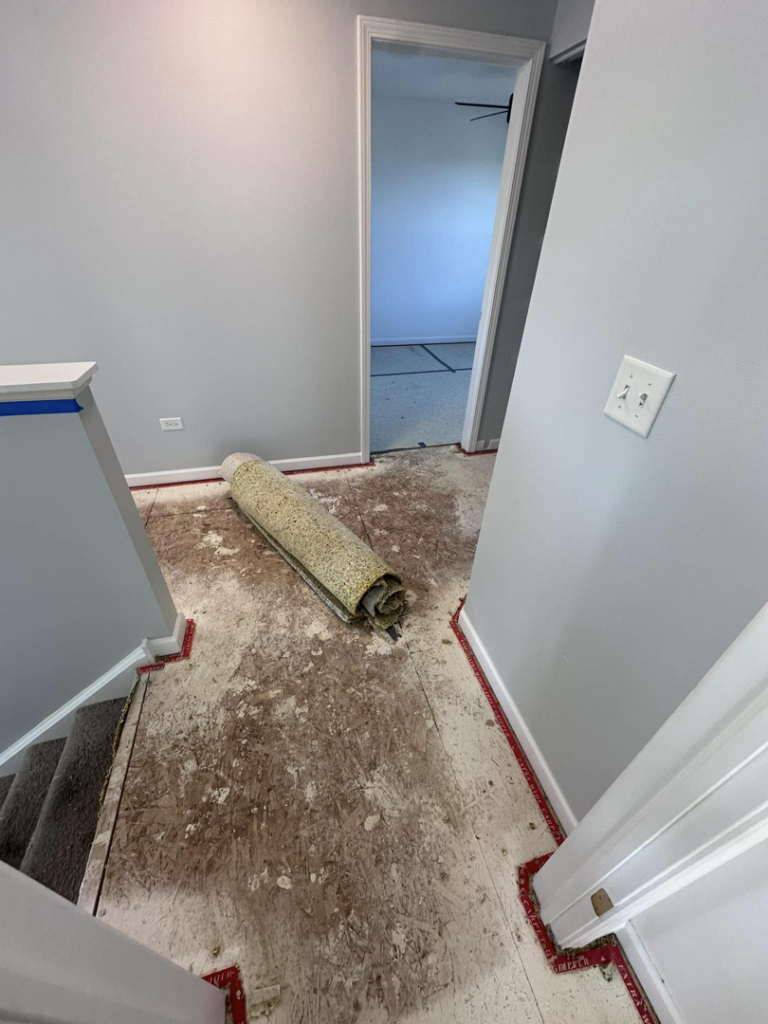 A hallway with old carpet removed and rolled up, showing subfloor, by J&A Flooring Masters Corp. in Joliet, IL.