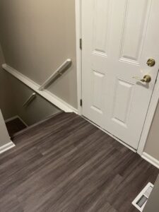 A newly installed dark plank flooring in a hallway leading to carpeted stairs by A&N Install in Rochester, NY.