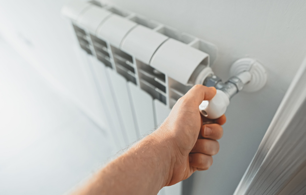 A hand adjusting a radiator valve, representing heating system service by Comfy Cave Heating and Air Conditioning in Arvada, CO.