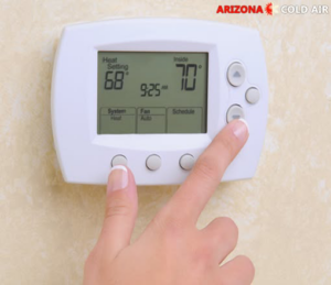 A hand adjusting a digital thermostat for heating and cooling at Arizona Cold Air in Mesa, AZ.