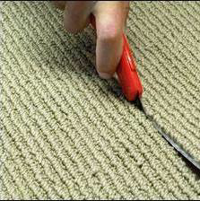 A close-up of a hand using a utility knife to cut carpet, demonstrating installation work by Eatherton's Fashion Floors in St. Louis, MO.