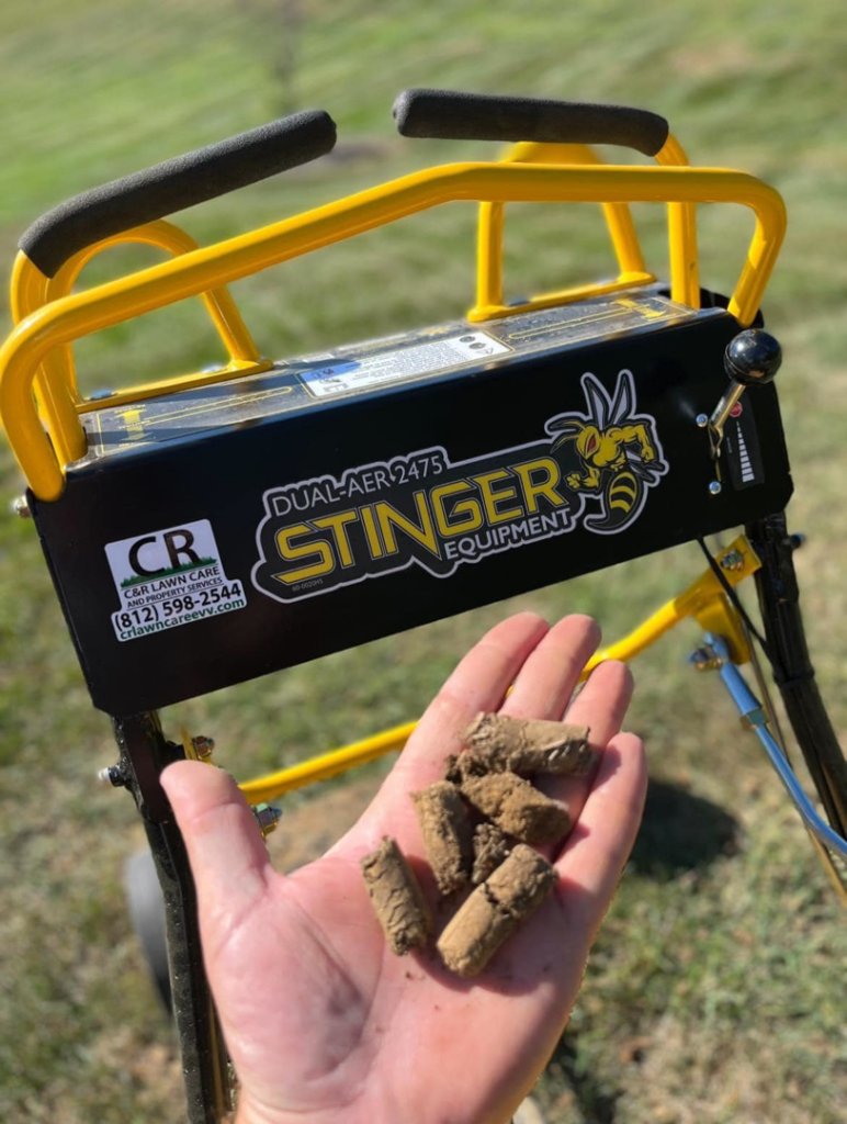 A hand holding soil plugs from lawn aeration, with a Stinger Equipment aerator and C&R Lawn Care and Property Services branding in Evansville, IN.