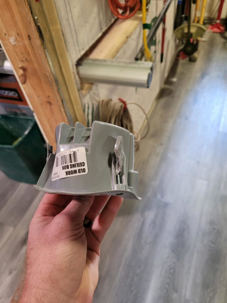 A hand holding an old work ceiling box, a common electrical component used by 12 Stones Electric in Davenport, IA.