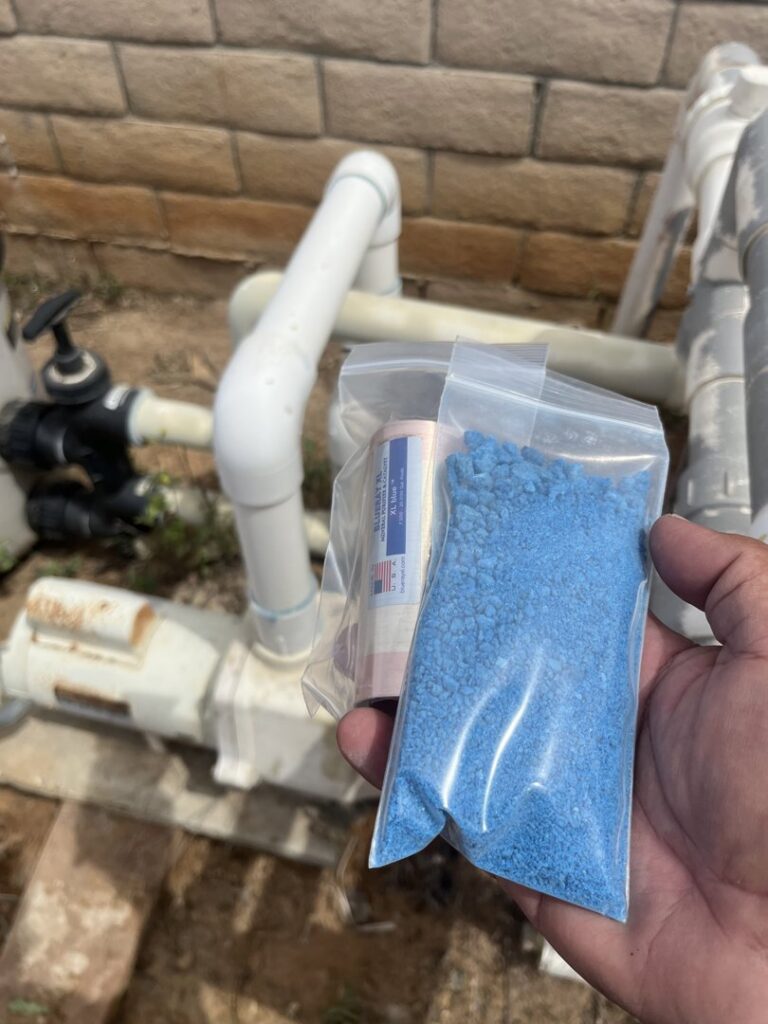 A hand holding bags of blue granular pool chemicals, used for treatment by Good Guy Pool Service in Moreno Valley, CA.