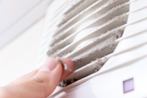 A hand removing a large clump of dust and lint from a dirty air vent, showing the need for cleaning by Air Doctor Duct Cleaning & Lining in Tulsa, OK.