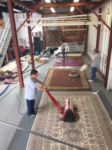 Workers hand-washing a large oriental rug with brushes and water at Demanes Oriental Rugs in Peoria, IL