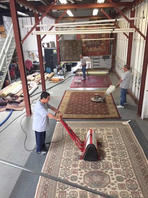Workers hand-washing a large oriental rug with brushes and water at Demanes Oriental Rugs in Peoria, IL