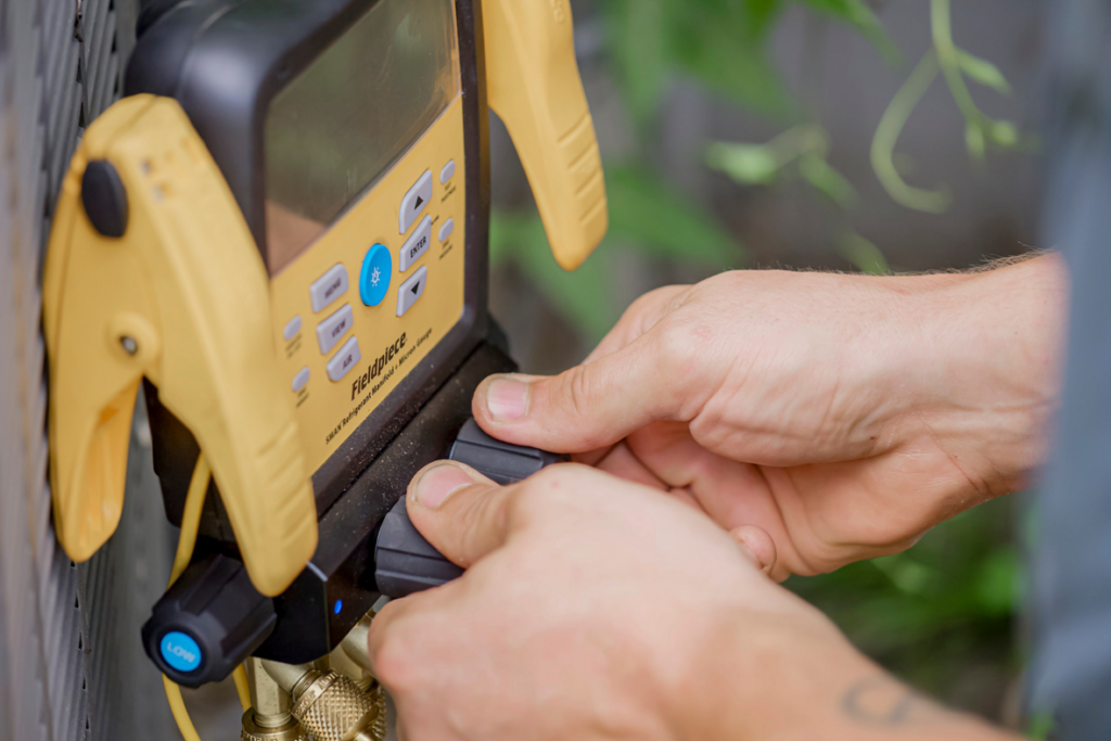 Hands adjusting a digital manifold gauge connected to an HVAC unit by On the Spot Heating and Cooling in Overland Park, KS.