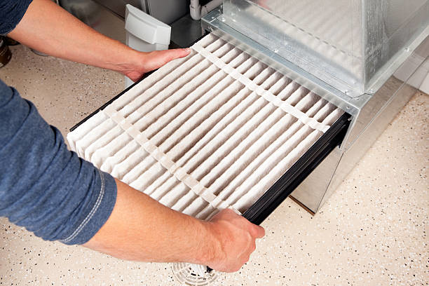 Hands changing a dirty furnace air filter, a key HVAC maintenance service by Cleveland Air Comfort in Solon, OH.