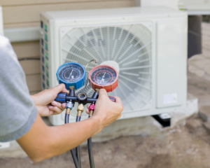 Hands holding HVAC manifold gauges in front of an outdoor air conditioning unit for Chrismon Heating & Cooling in Greensboro, NC.