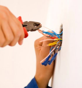 Hands using pliers to strip or cut electrical wires coming out of a wall, demonstrating work by Your Gilbert Electrician in Gilbert, AZ.