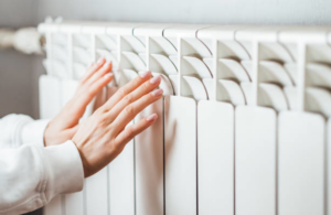 Hands touching a warm heating radiator, representing heating services from Infinity Heating & Cooling by Rivera in Kenosha, WI.