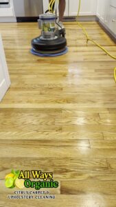 A professional cleaning technician operating a floor cleaning machine on a hardwood floor by All Ways Organic Citrus Carpet & Upholstery Cleaning in Wilmington, NC.