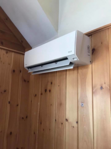 A white mini-split heat pump unit installed on a rustic wooden wall, maintained by Winks Heat Pump Cleanings in Bangor, ME