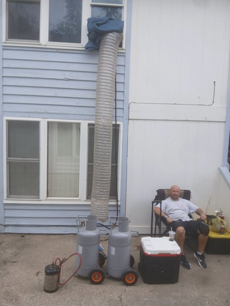 A man observing a heat treatment setup with propane tanks and ducting outside a home by All Seasons Pest Control LLC in Topeka, KS.