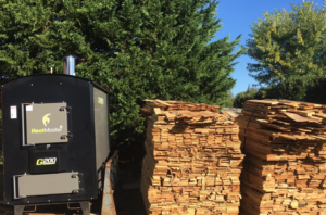 A HeatMaster C200 outdoor wood furnace system next to stacks of wood by East Tennessee Wood Heat in Knoxville, TN.