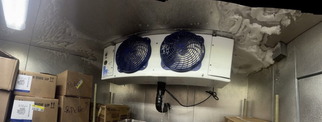 A heavily frosted evaporator unit inside a commercial walk-in freezer, indicating a service need for Four Corners Service Co. in Farmington, NM.