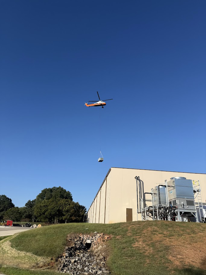 A helicopter lifting a large HVAC unit onto a commercial building for Commercial Air Condition Service, Inc. in Greenville, SC