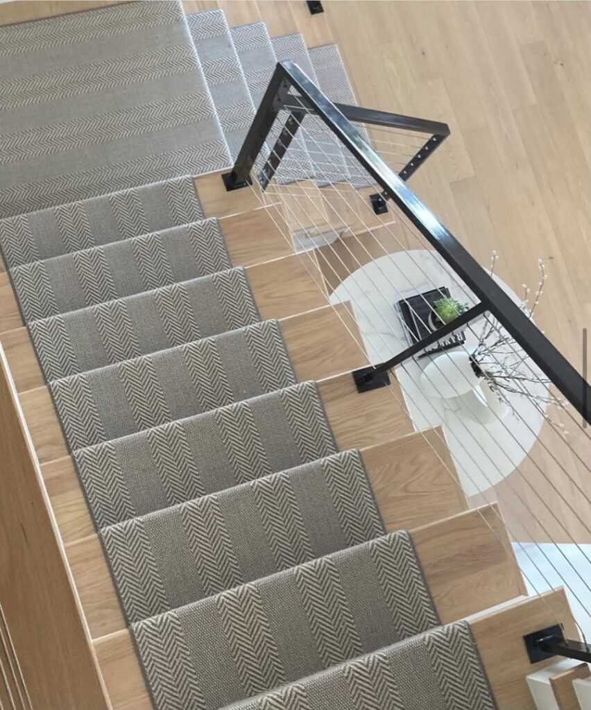 A modern herringbone pattern carpet runner installed on a wooden staircase by Floors Next Day in Austin, TX.
