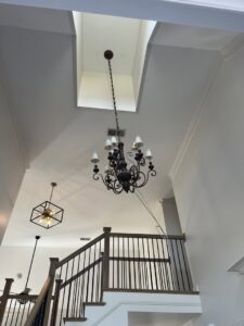 An electrician servicing a chandelier in a high-ceiling entryway using a rope system, by Shocking Solutions in Knoxville, TN.
