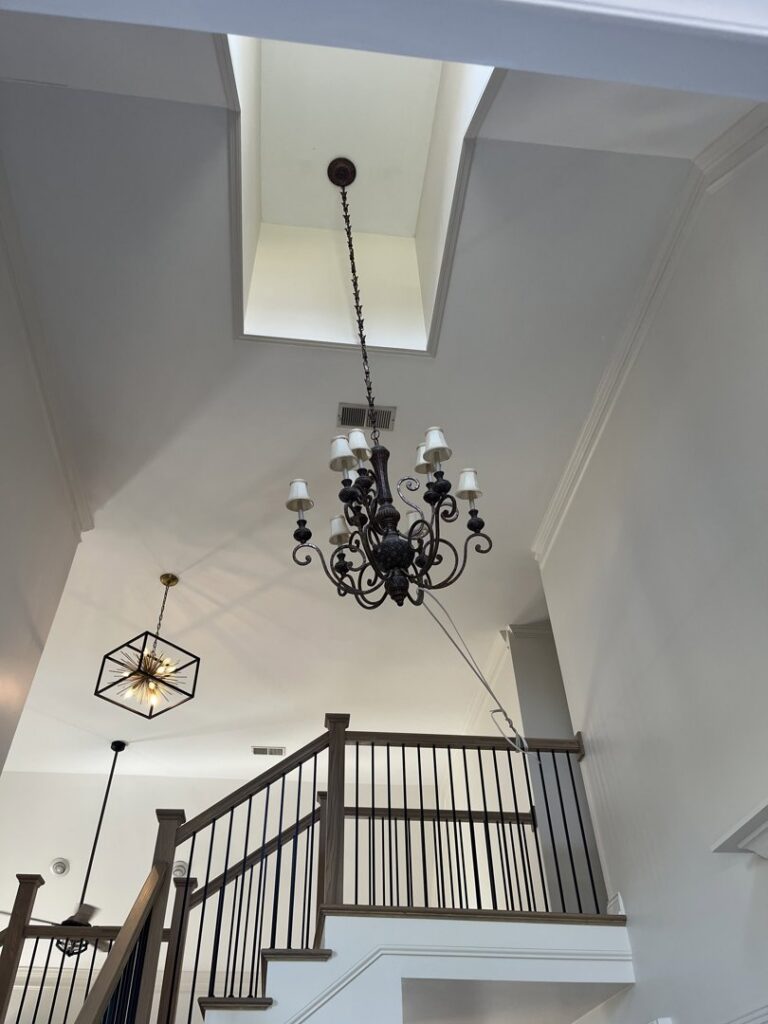 An electrician servicing a chandelier in a high-ceiling entryway using a rope system, by Shocking Solutions in Knoxville, TN.
