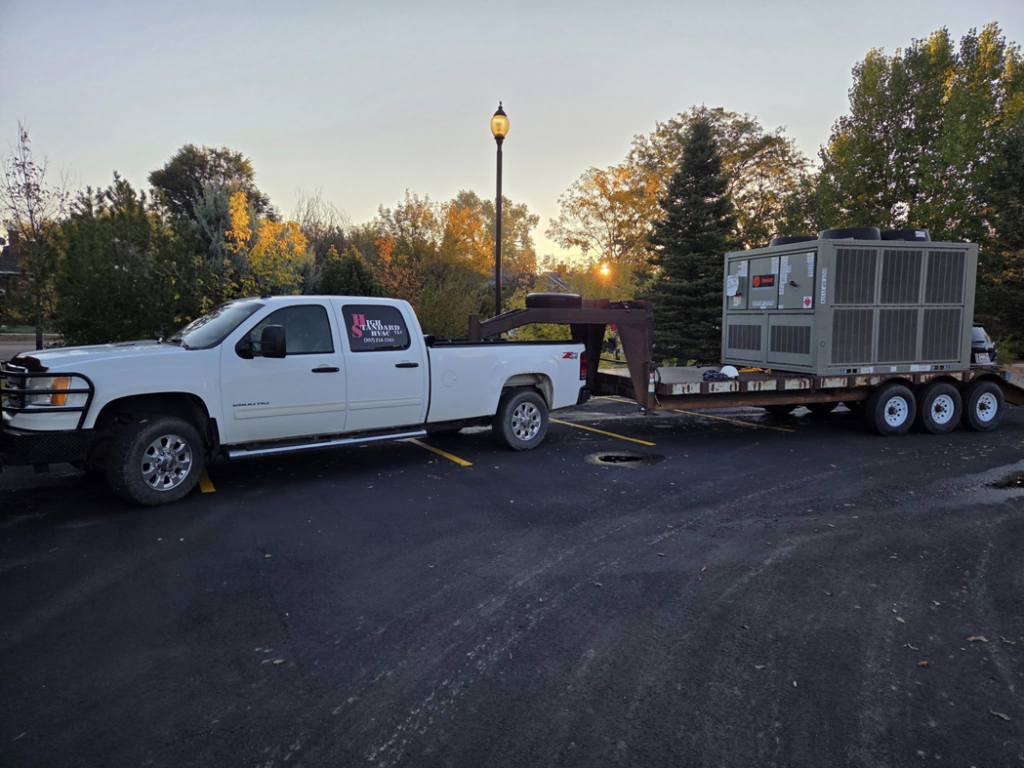 A High Standard HVAC LLC truck transporting a large commercial HVAC unit on a trailer in Cheyenne, WY.