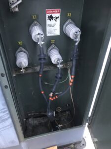 An open high-voltage electrical transformer box with warning labels, showing work by Premier Electric LLC in Palmer, AK.