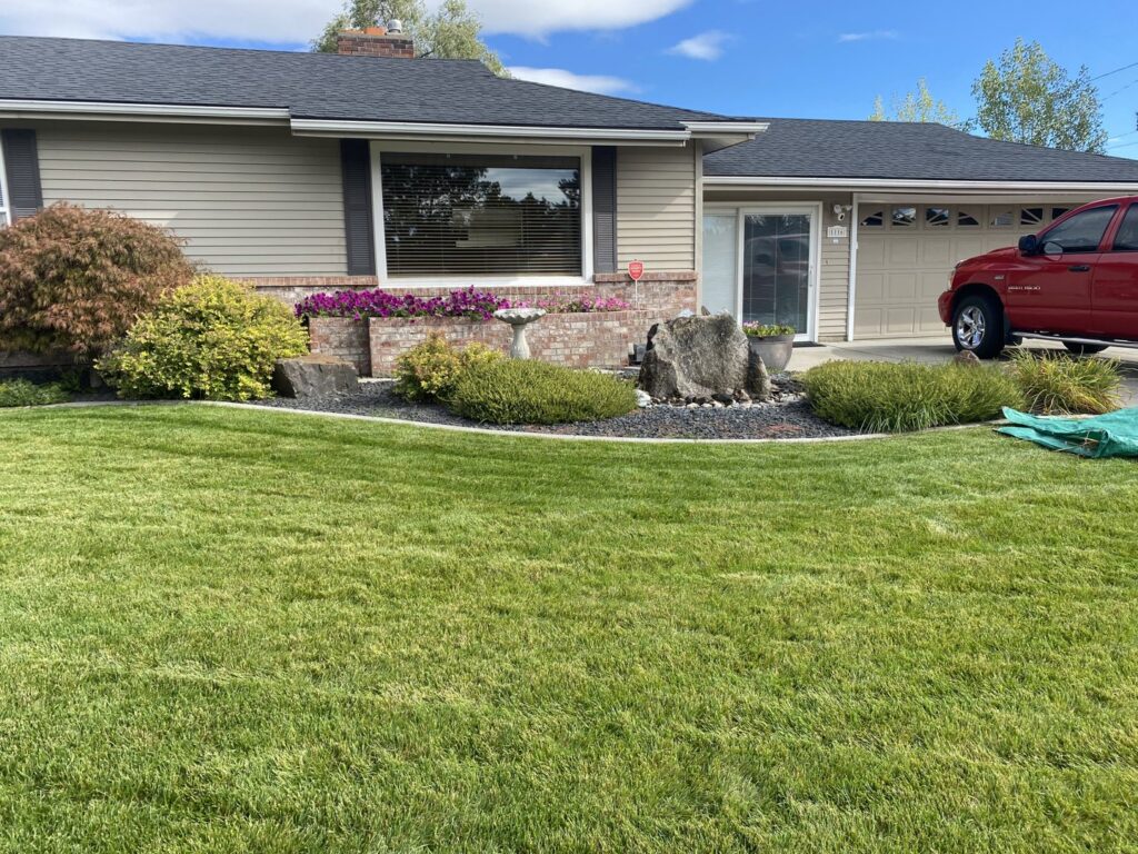 A residential home with a vibrant green lawn and well-kept landscape beds, reflecting expert lawn care from McLain Lawn & Landscape in Spokane, WA.
