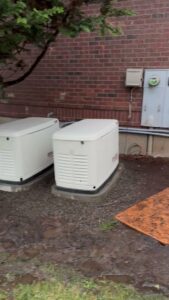Home standby generators installed outside a brick building, showcasing generator services by Mountain Coast Electric in Salem, OR