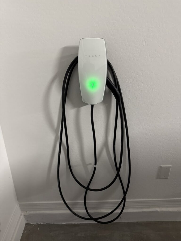 A home Tesla electric vehicle charger professionally installed on a white wall by Castle Electrical & Lighting in Scottsdale, AZ.