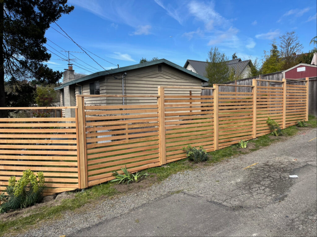 A modern horizontal slat fence installed along a sloped yard by Helmco Fences in Seattle, WA.