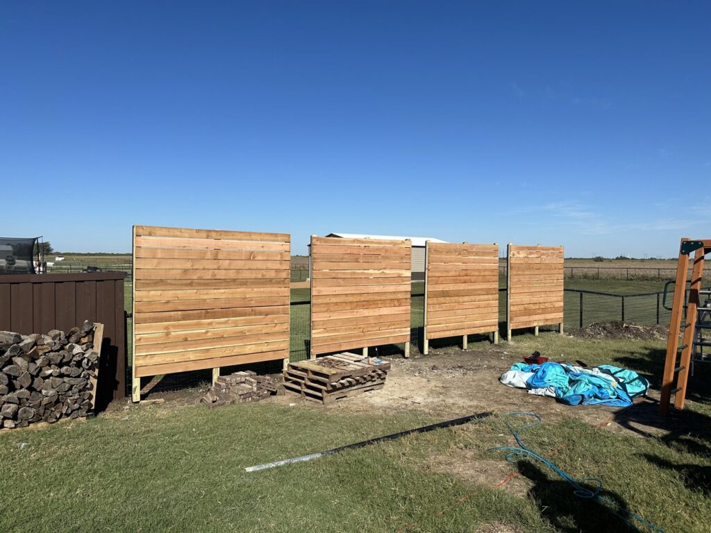 Multiple sections of a modern horizontal slat wood fence under construction in a grassy field by NTX-Exterior Services in Dallas, TX.