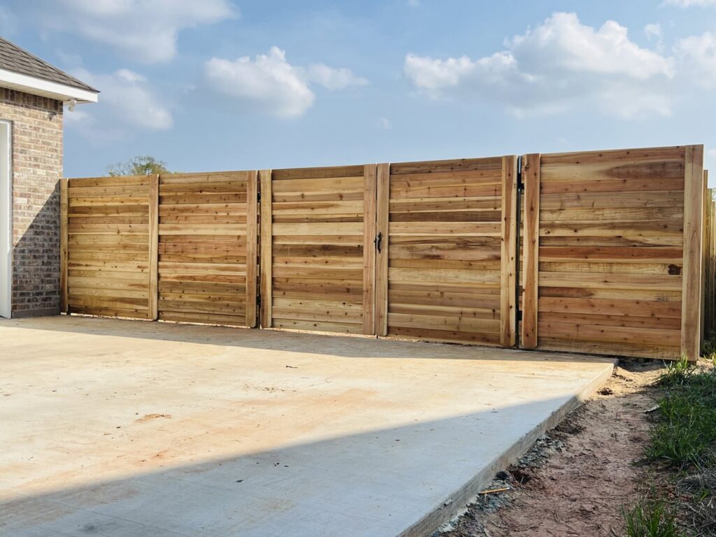 A newly installed horizontal slat wood fence with a matching gate next to a concrete patio by Capitol Fencing in Baton Rouge, LA.