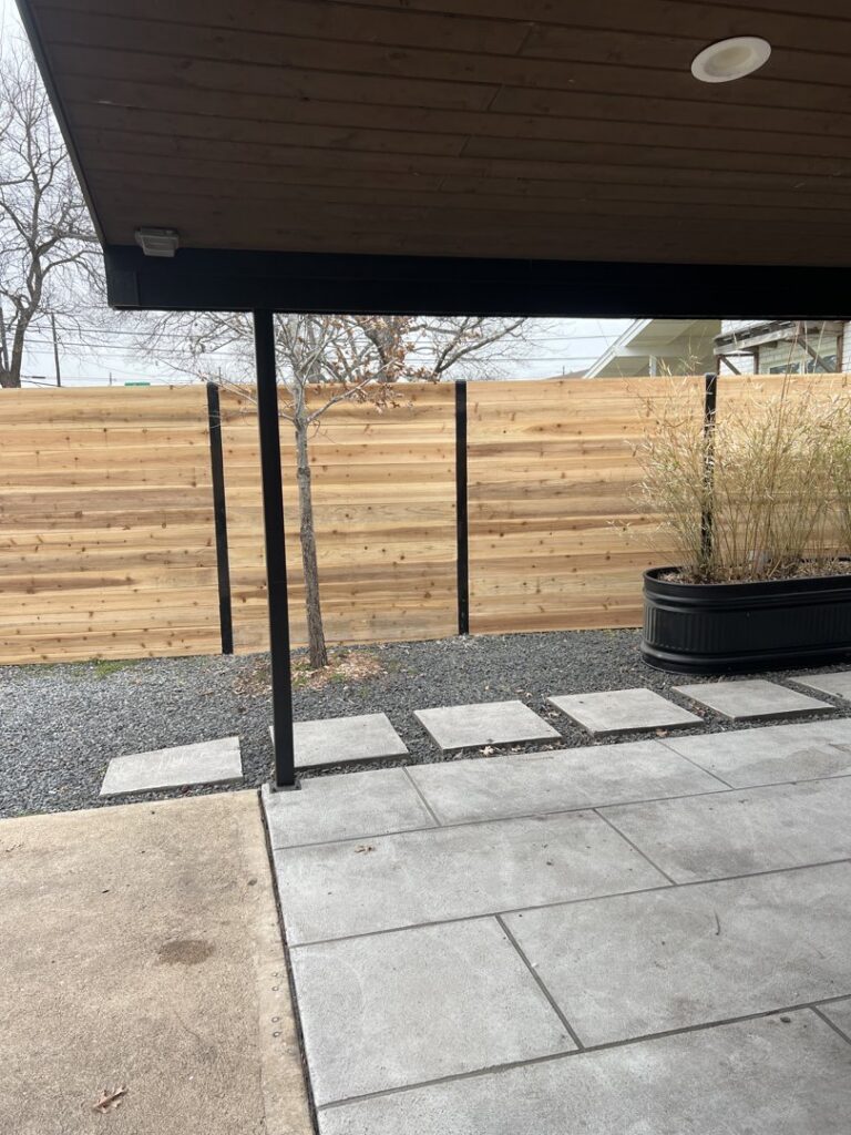A modern horizontal slat wood fence with black posts next to a patio by Good Neighbor Fencing and Construction in Austin, TX.