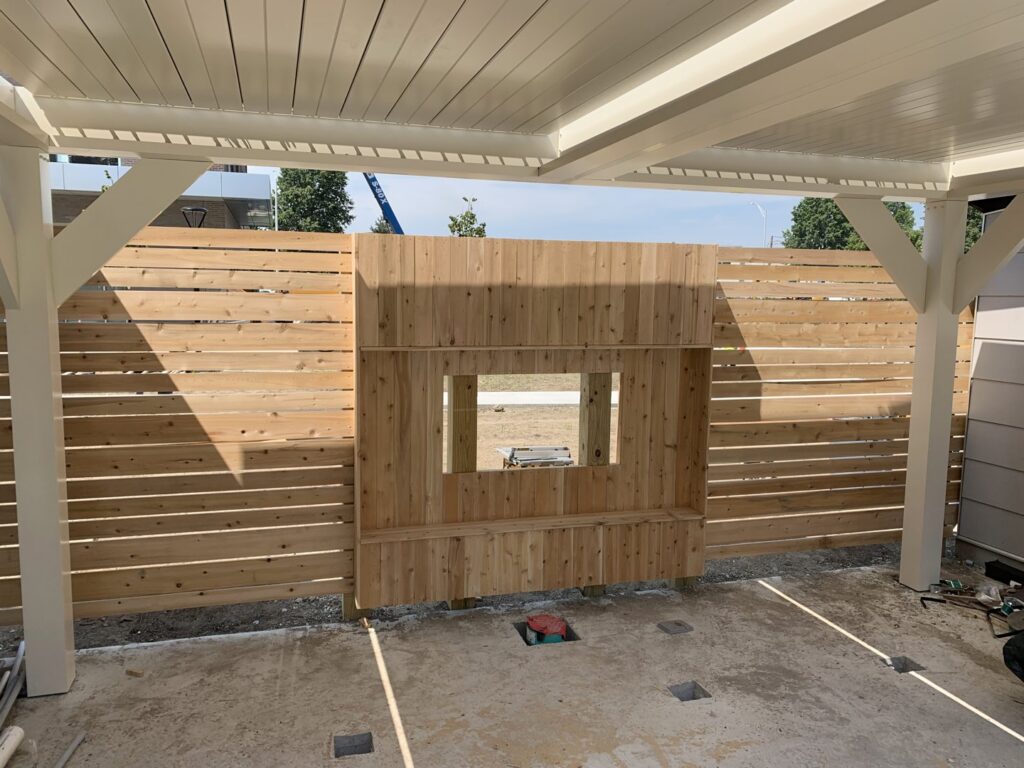 Custom horizontal slat wood fence with a window opening under a patio cover by Louis Fence installations & repairs in Fall River, MA