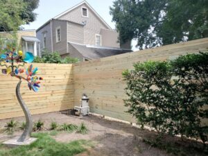 A newly installed horizontal slat wooden fence next to a house and pool pump by 5-Alarm Fence Company in New Orleans, LA.